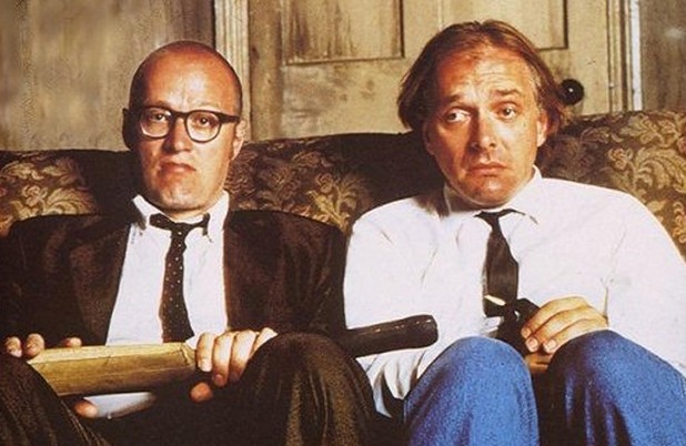 Rik Mayall and Ade Edmondson, of the TV Show Bottom, sitting on a couch. Ade Edmondson is holding a cricket bat, and Rik Mayall is pulling a face