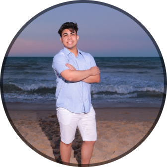 Foto do Pedro Euzebio sorrindo de braços cruzados usando uma camisa social azul claro com o fundo o mar aberto.