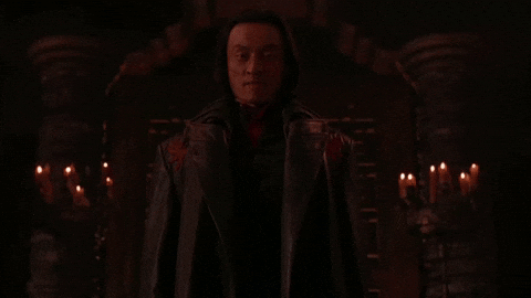 Darkly lit dungeon-y scene; hooded figure with visible face saying 'flawless victory'