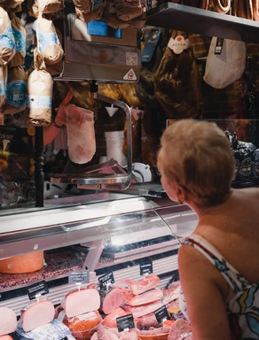 A sausage counter. A hand displays a ham slice to a customer.