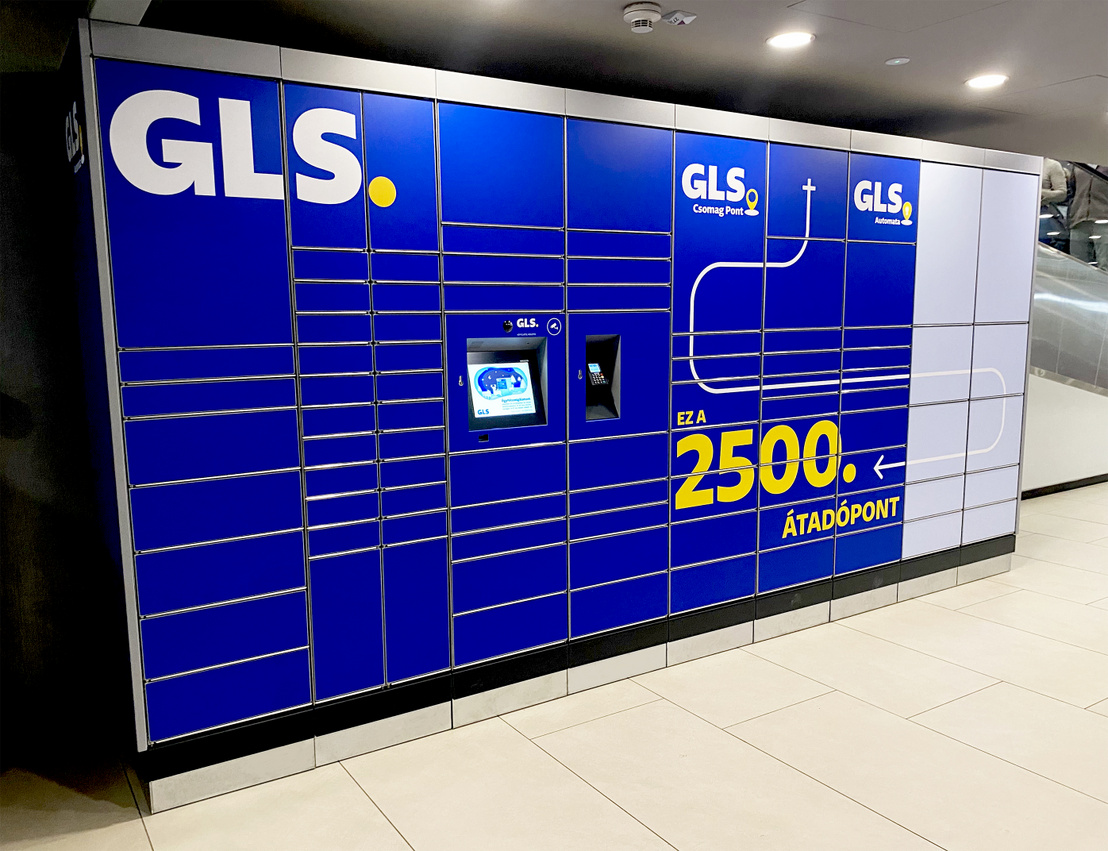 A blue GLS package locker with multiple compartments and digital screens, prominently featuring the number 2500 and directional text. The locker is located indoors with bright overhead lighting.