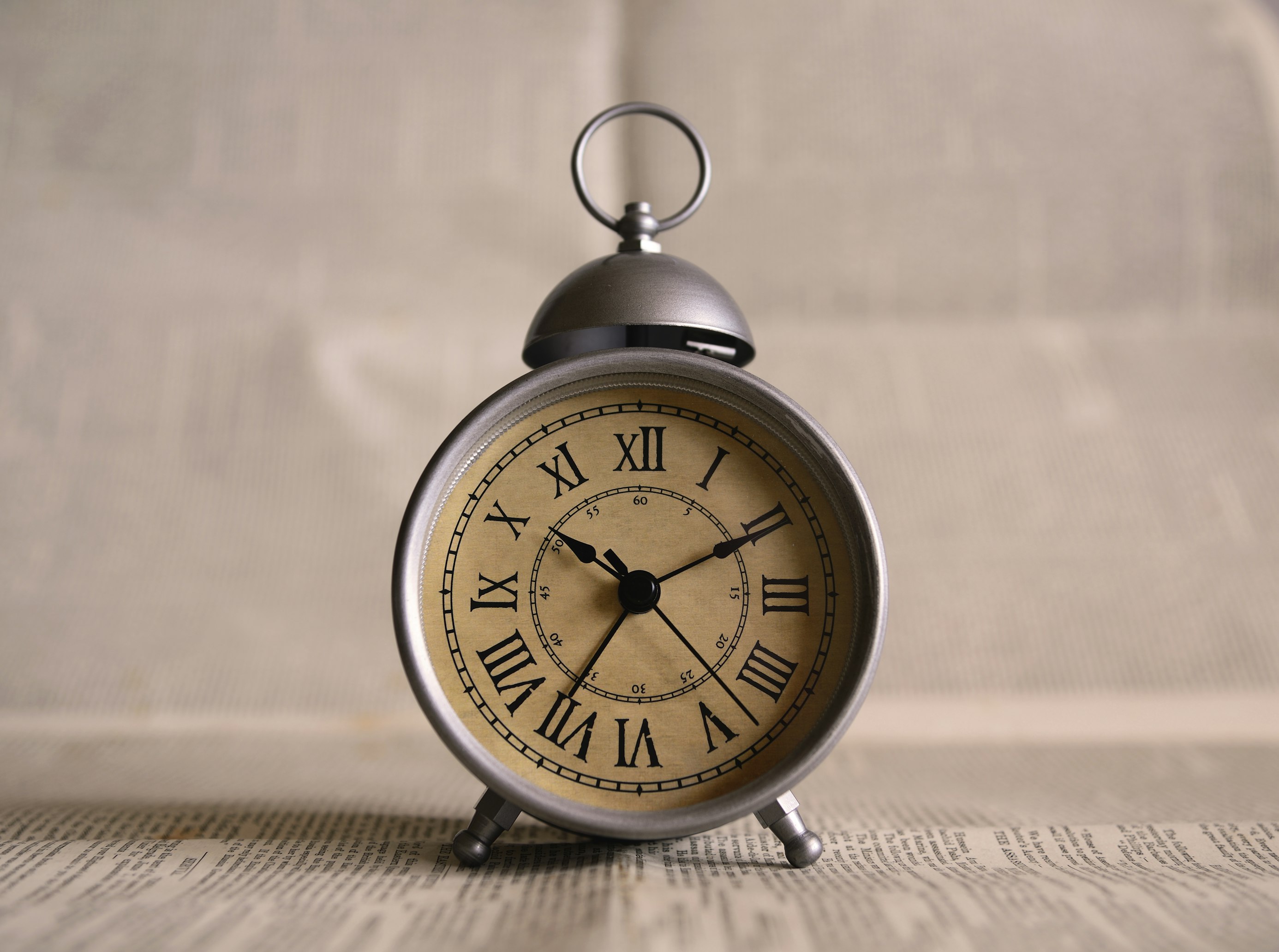 Vintage-style alarm clock with Roman numerals on its face, set on a surface covered with newspaper, with a blurred background.