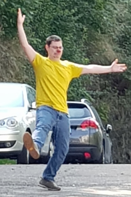 A man with a red nose. He holds his hands as if he wanted to direct traffic. In the background there are cars.