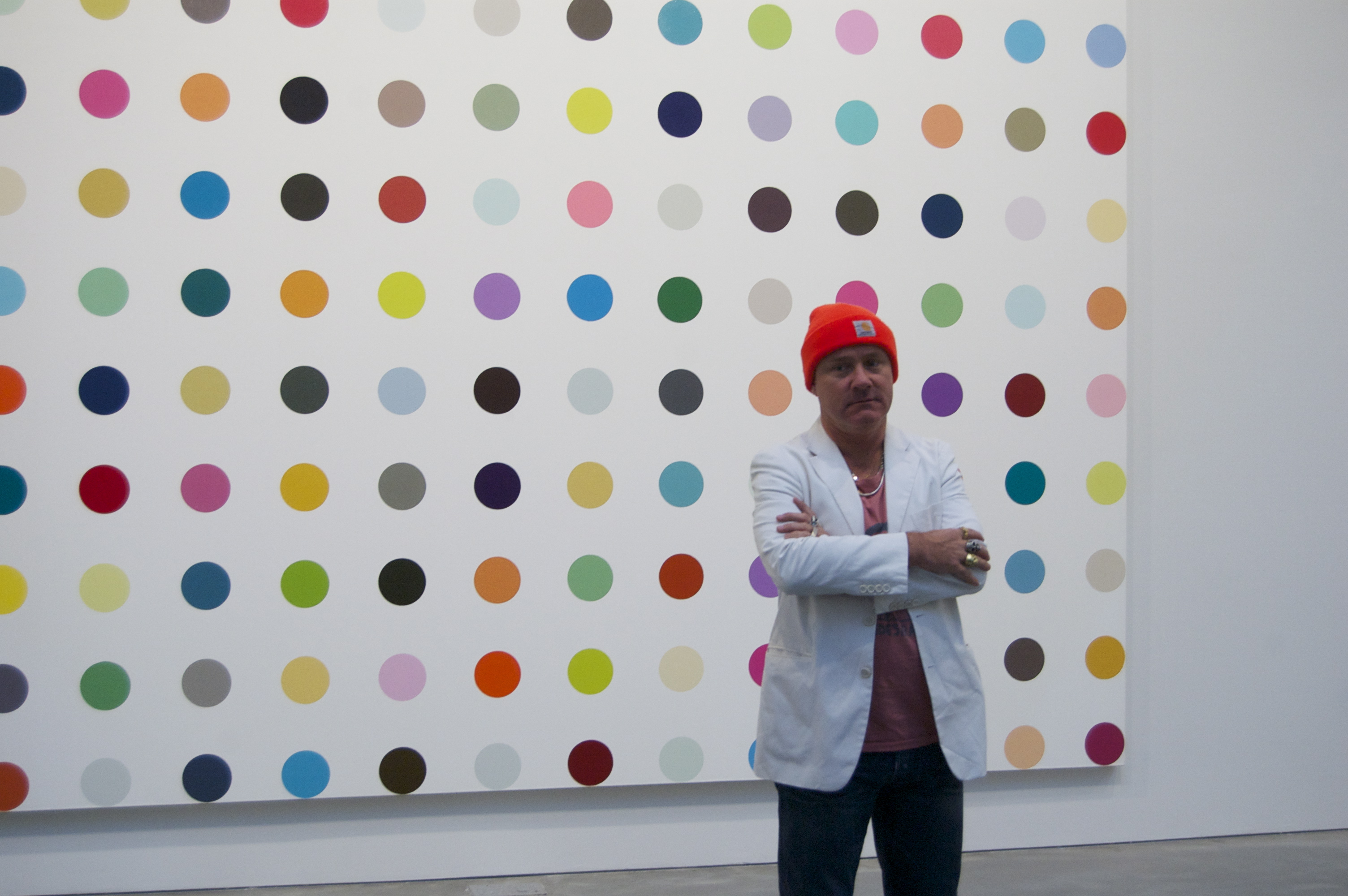 Damien Hirst standing in front of one of his spot paintings