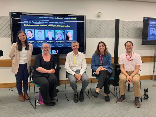 Alt: Picture of the keynote panel speakers. From left to right, standing, Jeniffer Ding. Seated: Kirstie Whitaker, Simon Reeve, Lauren Wool and Neil Chue Hong. Behind the speakers there is a screen with the title of the keynote: A