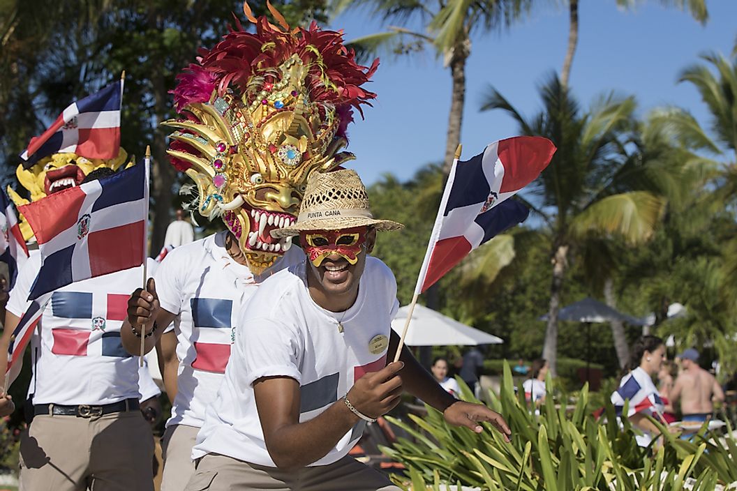 Independence Day celebrations in the Dominican Republic. Image is of a Dominican Republic citizen celebrating independence day in a half mask, smiling, waving a Dominican Republic flag and wearing a Dominican Republic flag t shirt. Editorial credit: Tina Andros / Shutterstock.com