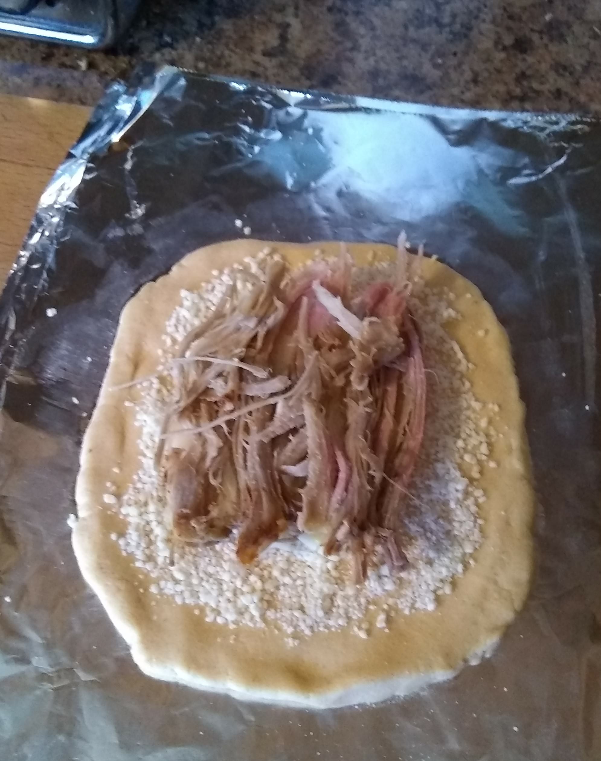 Image of dough covered in cheese and pork on tin foil