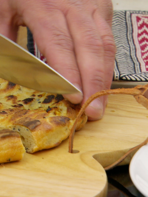 A hand holding a knife that is cutting bread