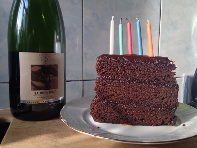 Slice of cake with five candles and a bottle of sparkling wine.