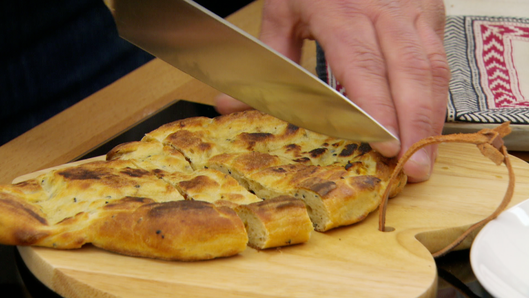 A hand holding a knife that is cutting bread