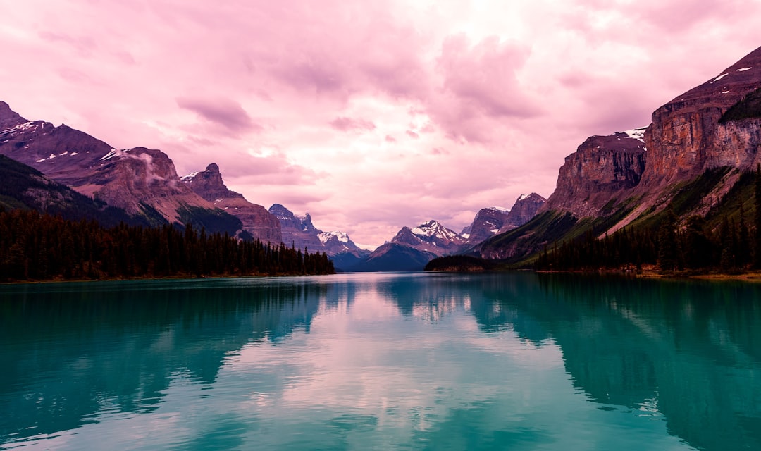 Turquoise lake reflecting snow-capped mountains under a soft pink cloudy sky