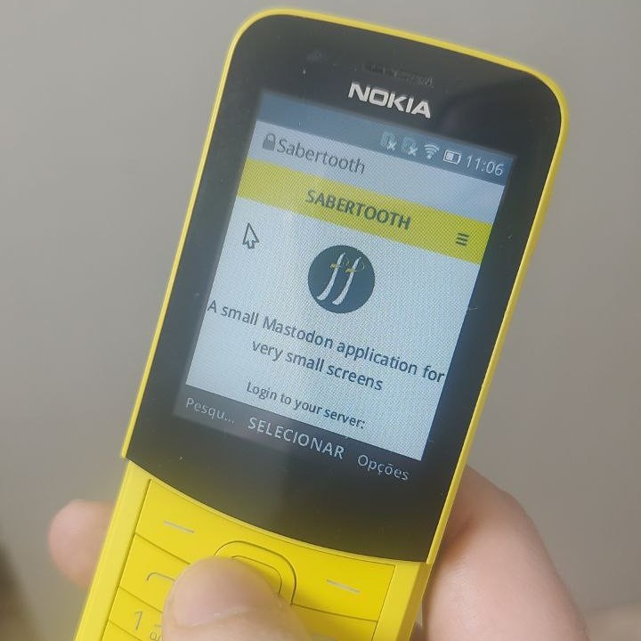 A color photography of a hand holding the phone. The phone is yellow, with black bezels around the screen. It has numeric physical keyboard and a small screen.