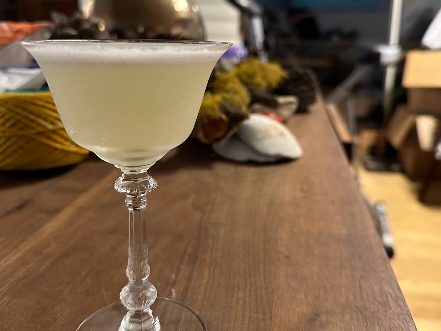 A pisco sour in a fancy crystal glass, with a thin layer of white foam on top